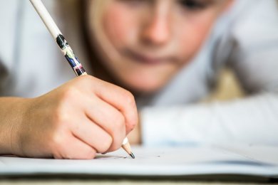 Едно момиче лежи по корем на пода и пише