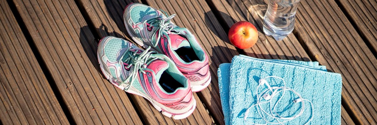 Спортни обувки, хавлиена кърпа, ябълка и бутилка вода върху дървени дъски