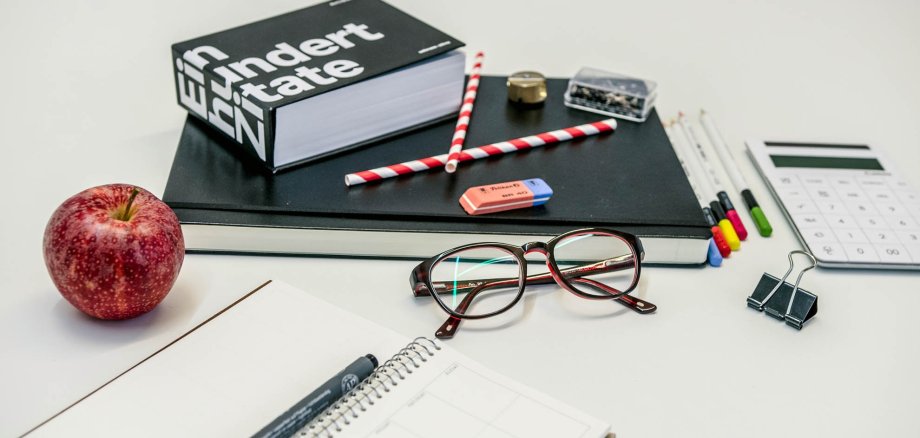 A calculator, glasses, a notepad, an apple and many other office supplies lie on a table.