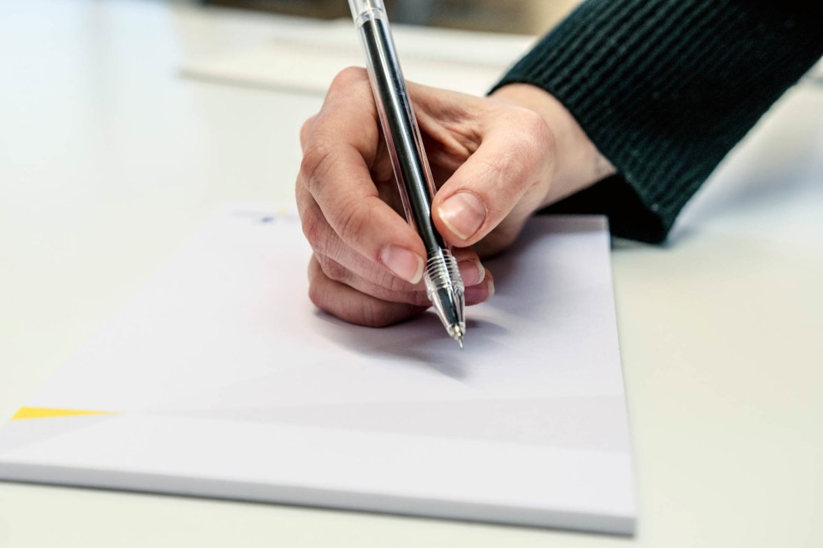 A person wants to write something down with the help of a pen and a pad.