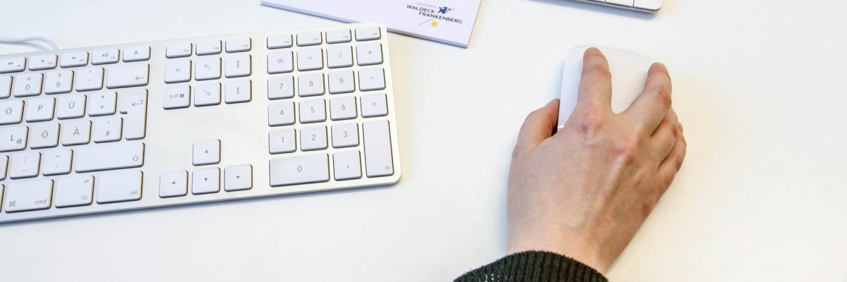 Someone is operating a computer mouse. Next to it is a keyboard and other office supplies.