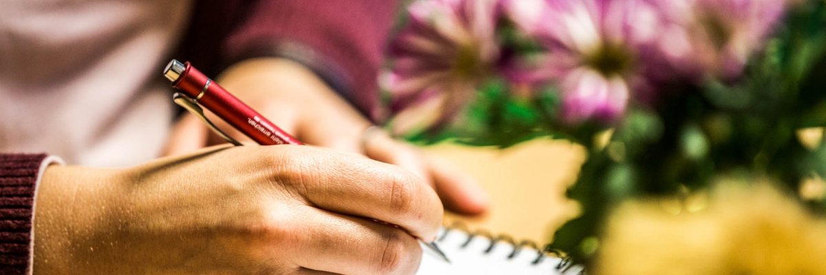 One hand holds a pen to take notes on a pad