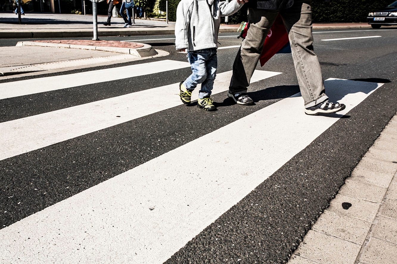 A small child and an adult walk across a zebra crossing