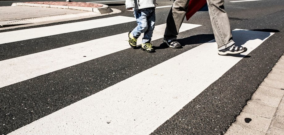 A small child and an adult walk across a zebra crossing