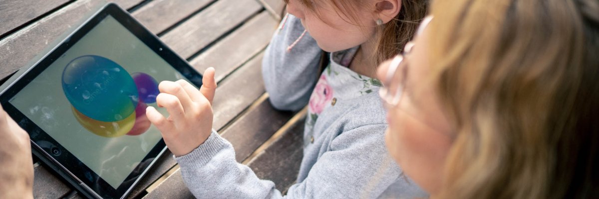 A young girl looks at a tablet, the mother looks on