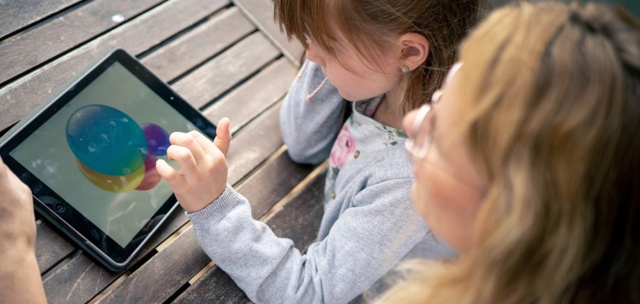 A young girl looks at a tablet, the mother looks on