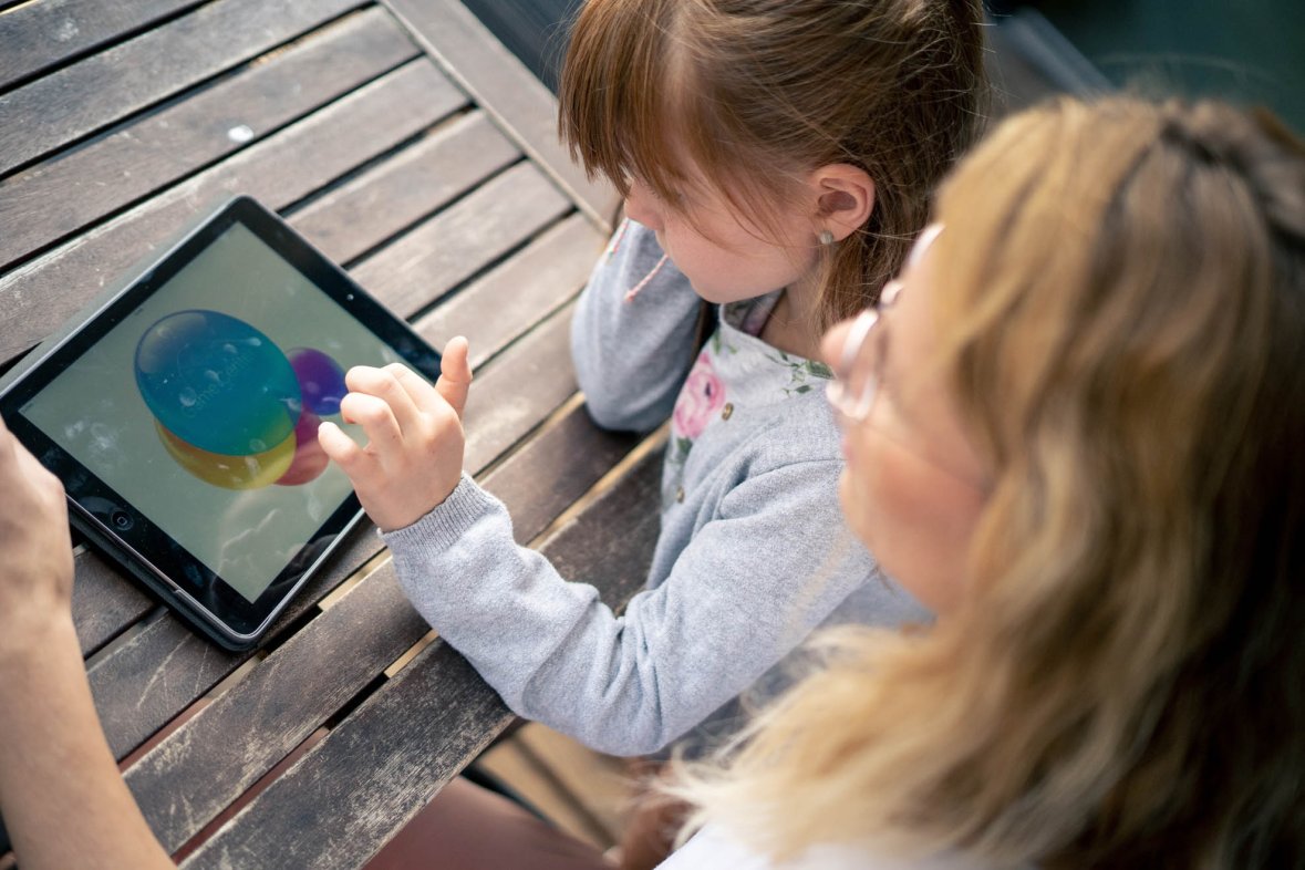 A young girl looks at a tablet, the mother looks on