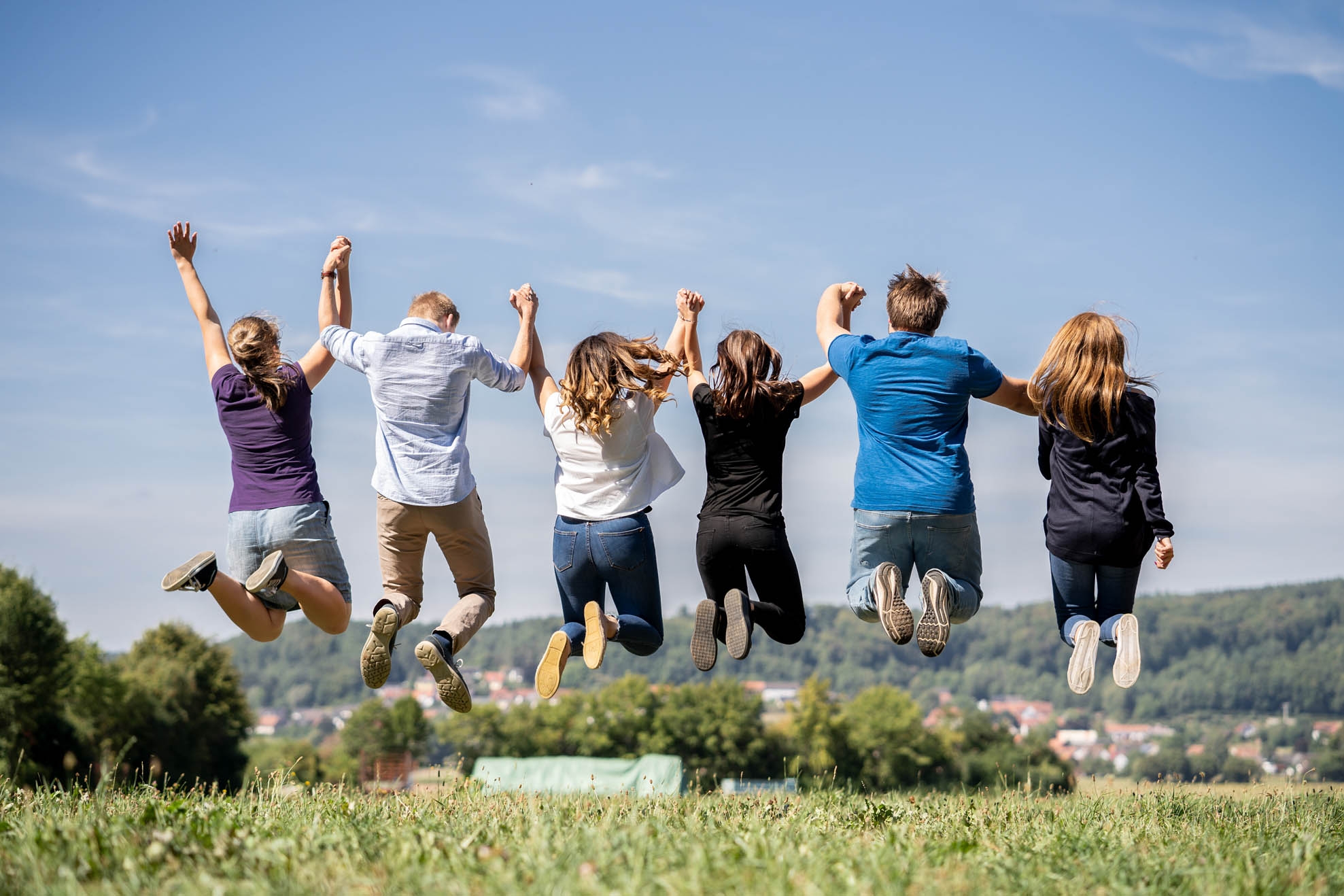 Air jump Six young people hold hands and do an aerial jump, back view
