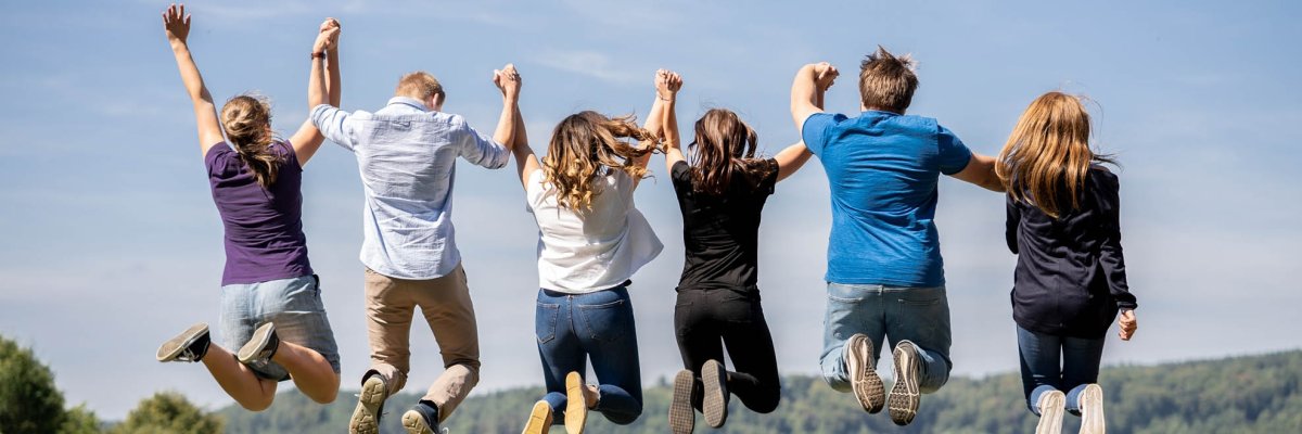 Six young people hold hands and do an aerial jump, back view