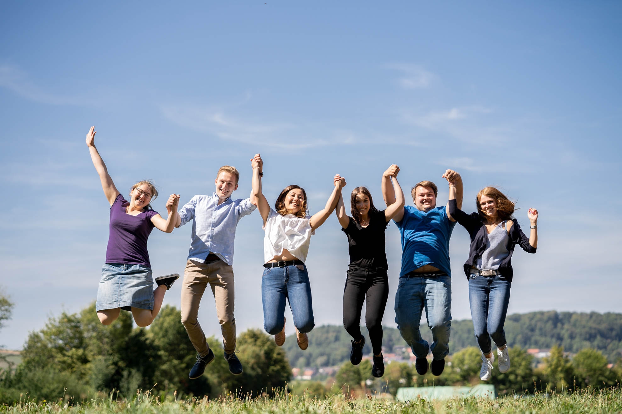 Six young people hold hands and make a leap in the air, front view