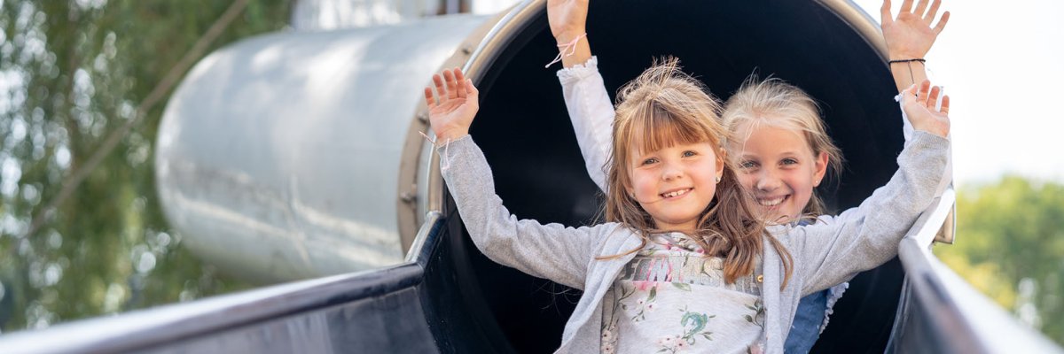 Two girls come sliding out of a slide tunnel