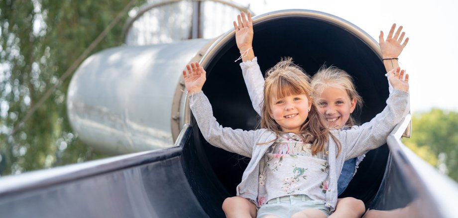 Two girls come sliding out of a slide tunnel