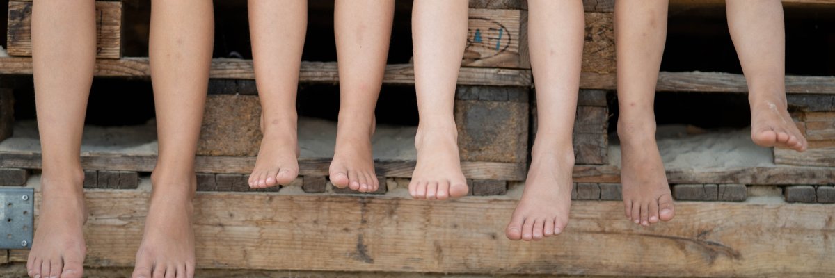 Four pairs of legs with bare feet on a bench