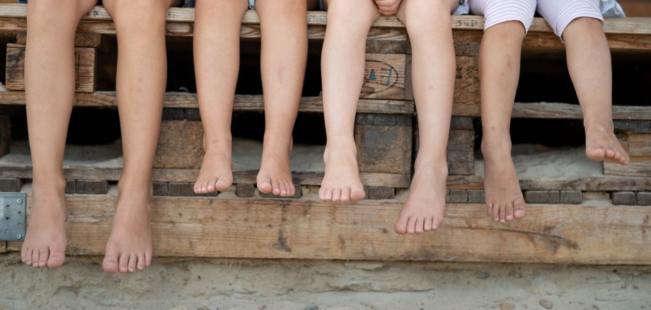 Four pairs of legs with bare feet on a bench