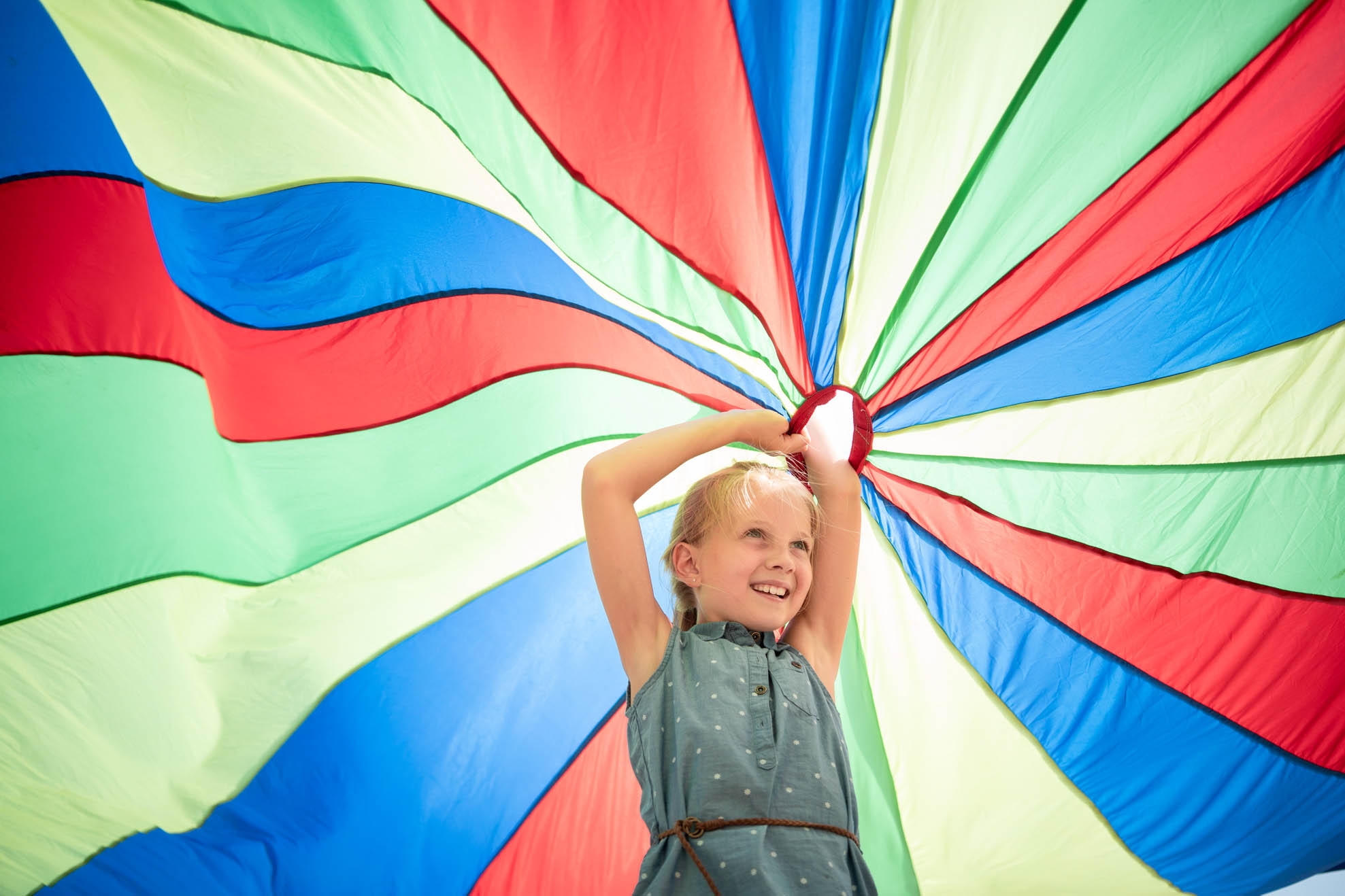 Parachute A girl stands under a colourful play parachute and holds it high