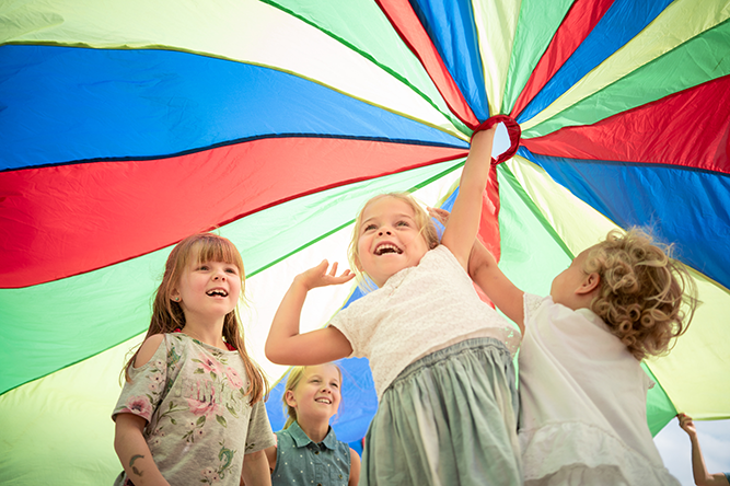 Parachute Four children stand under a colourful play parachute and hold it high