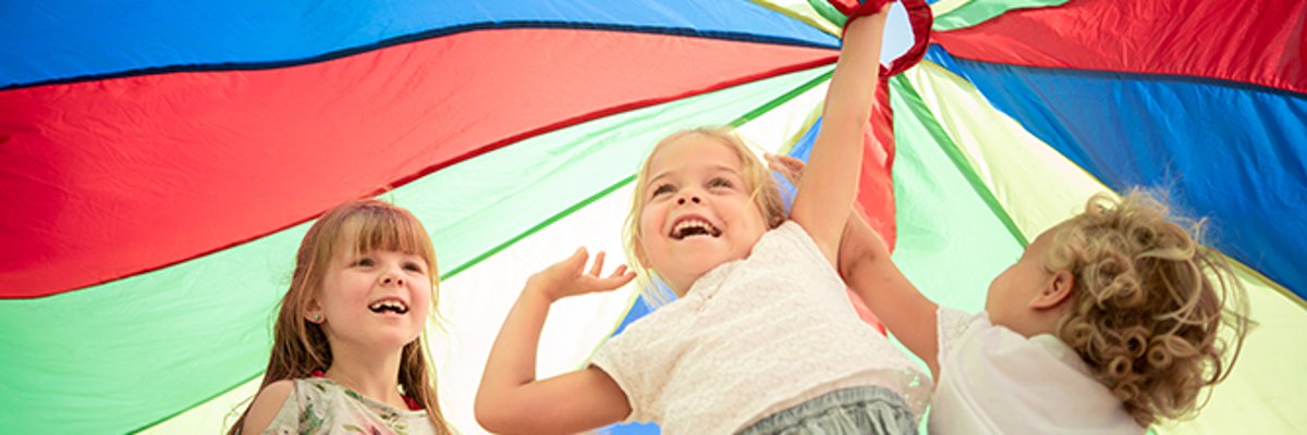 Four children stand under a colourful play parachute and hold it high