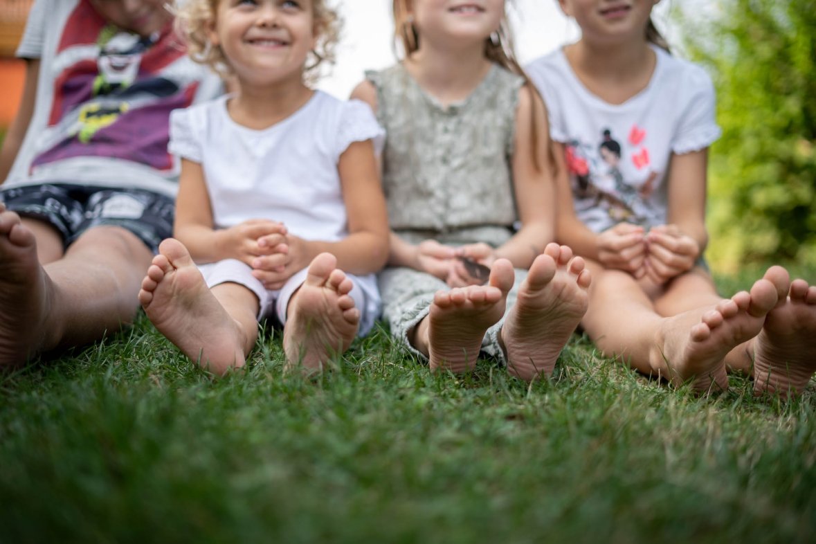 Four children sitting on the grass with bare feet