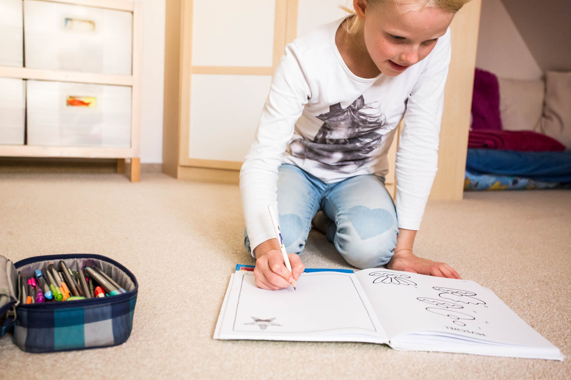 Painting A girl kneels on the floor and draws in a colouring book