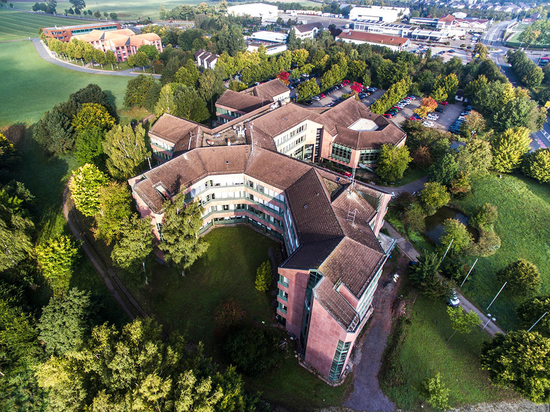 Aerial view of large red building surrounded by trees and meadows