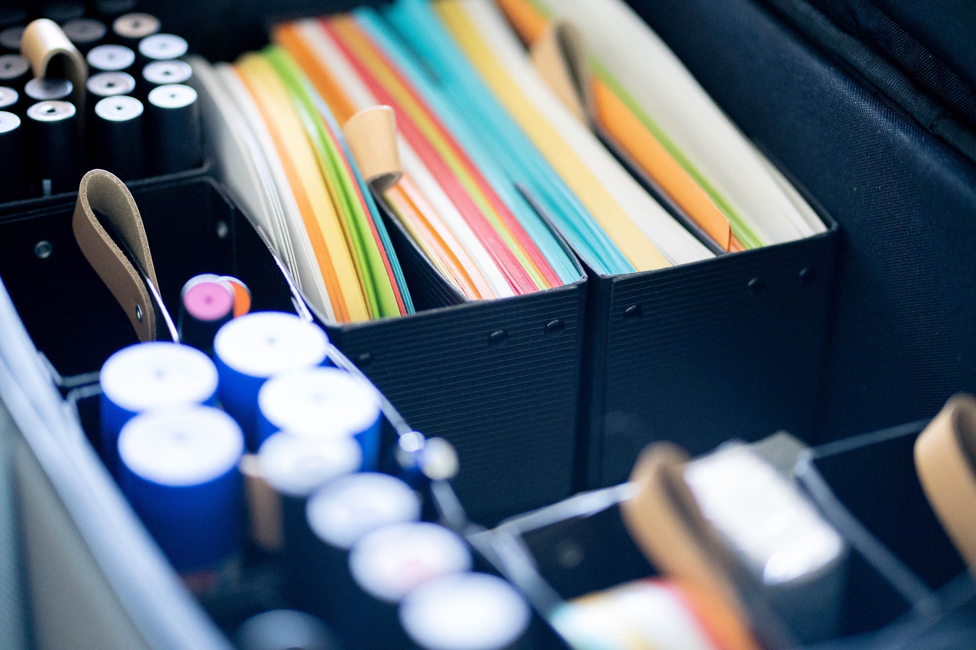 Colourful pieces of paper, thick pens and office supplies in a suitcase