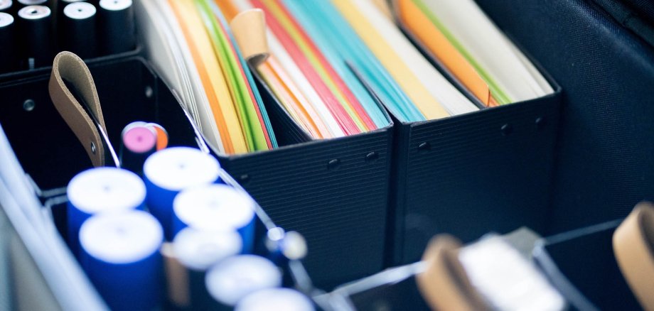 Colourful pieces of paper, thick pens and office supplies in a suitcase