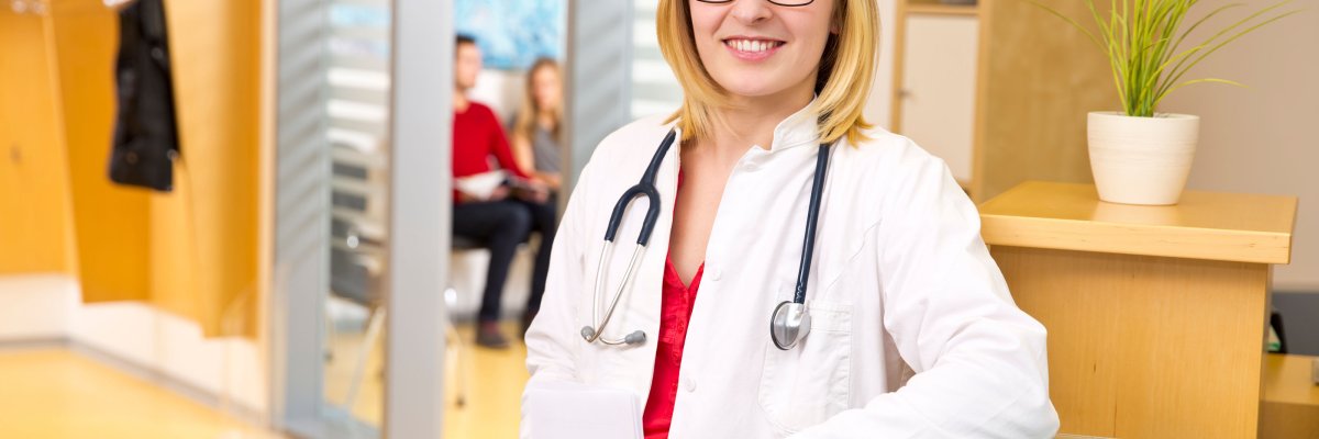 Smiling woman in doctor's coat with stethoscope around neck at reception of doctor's office