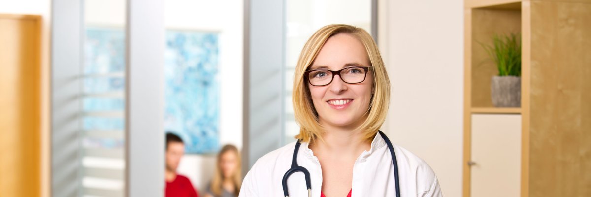 Smiling woman in a doctor's coat with stethoscope around her neck at the reception of a doctor's surgery