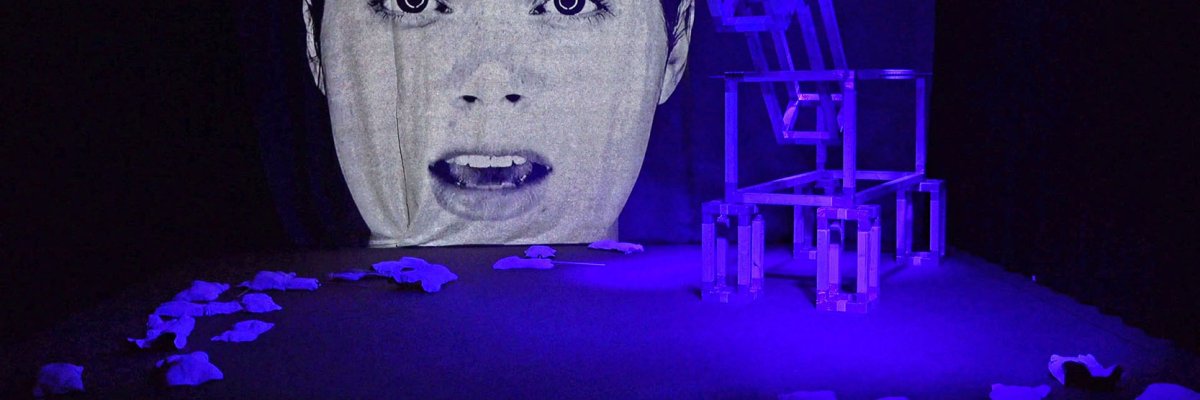 Oversized face of a young woman on a screen in front of dark blue lighting