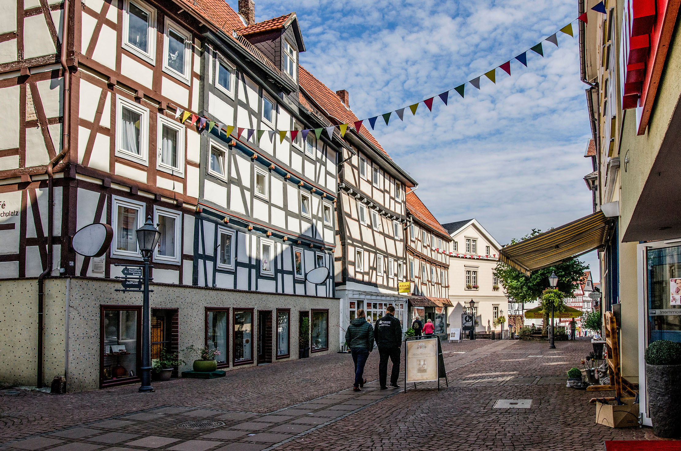Row of half-timbered houses with people on the street in front and a garland of flags at the level of the 2nd floor