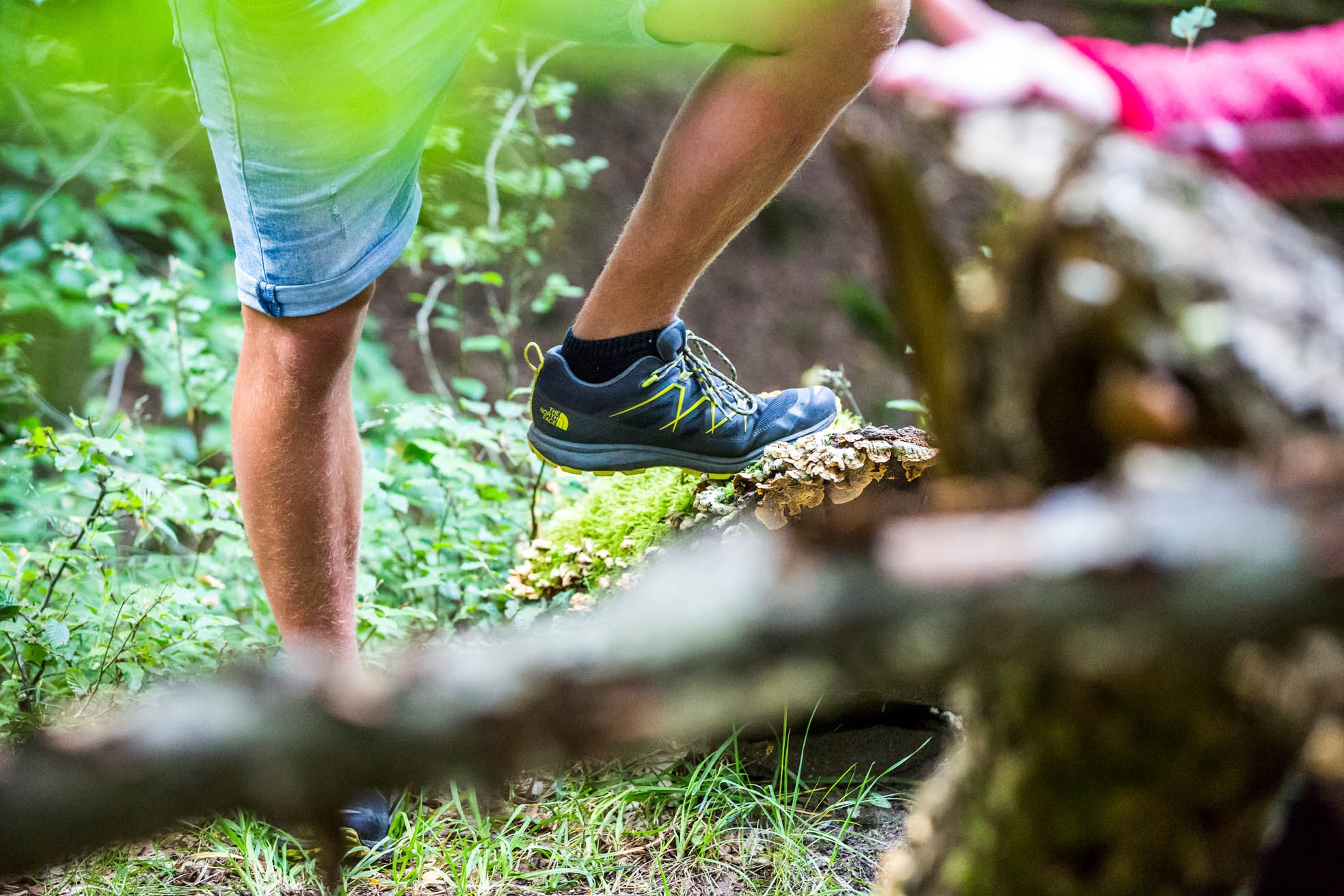 Man's legs in shorts, left foot in light hiking boot stands on a mushroom-covered tree stump