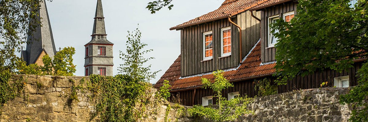 Spire and spire behind a stone wall, on the right a house roof protrudes above the wall