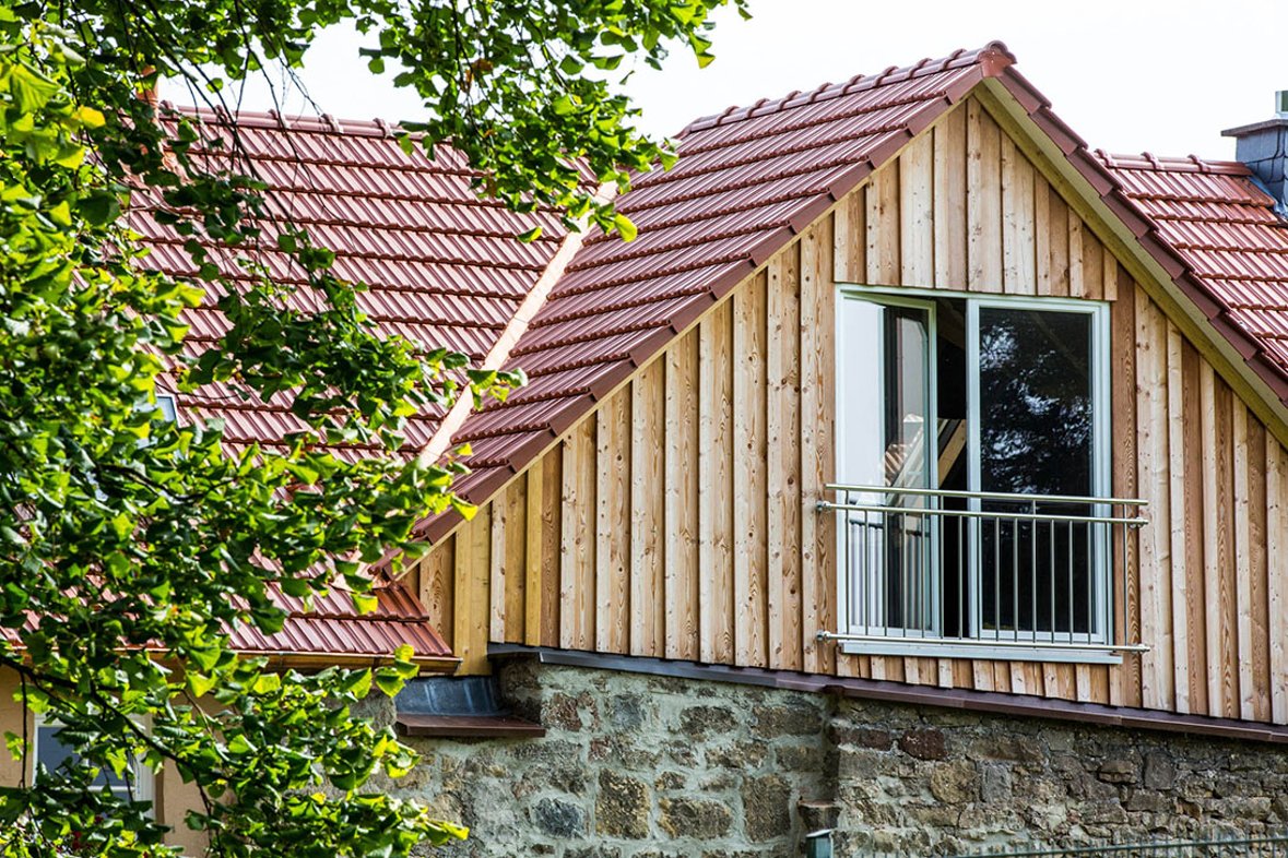House gable with large floor window behind a stone wall, on the right deciduous tree branches