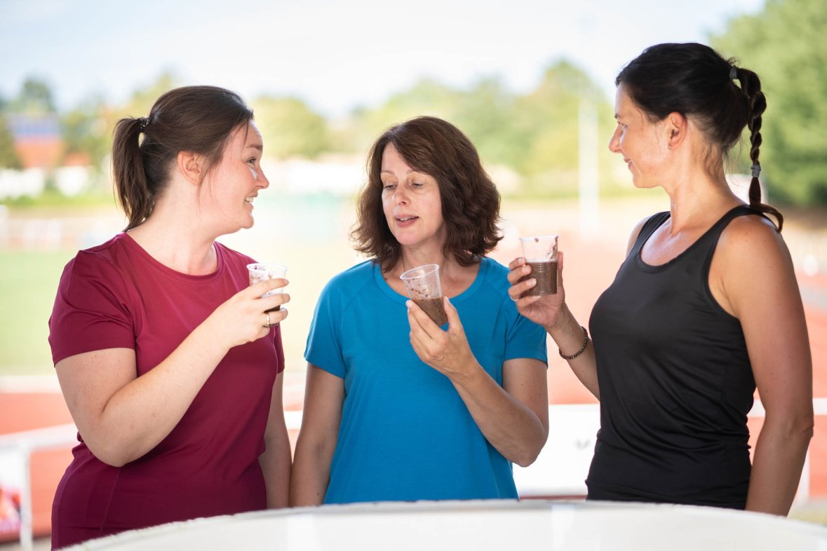 Three women in sportswear hold glasses with liquid in their hands