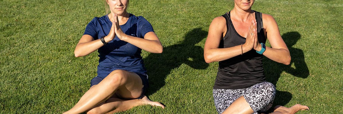 Two women sit in a yoga posture on the lawn