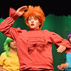 Jumping jack with tousled red hair and red overalls, colourfully dressed youths in the background