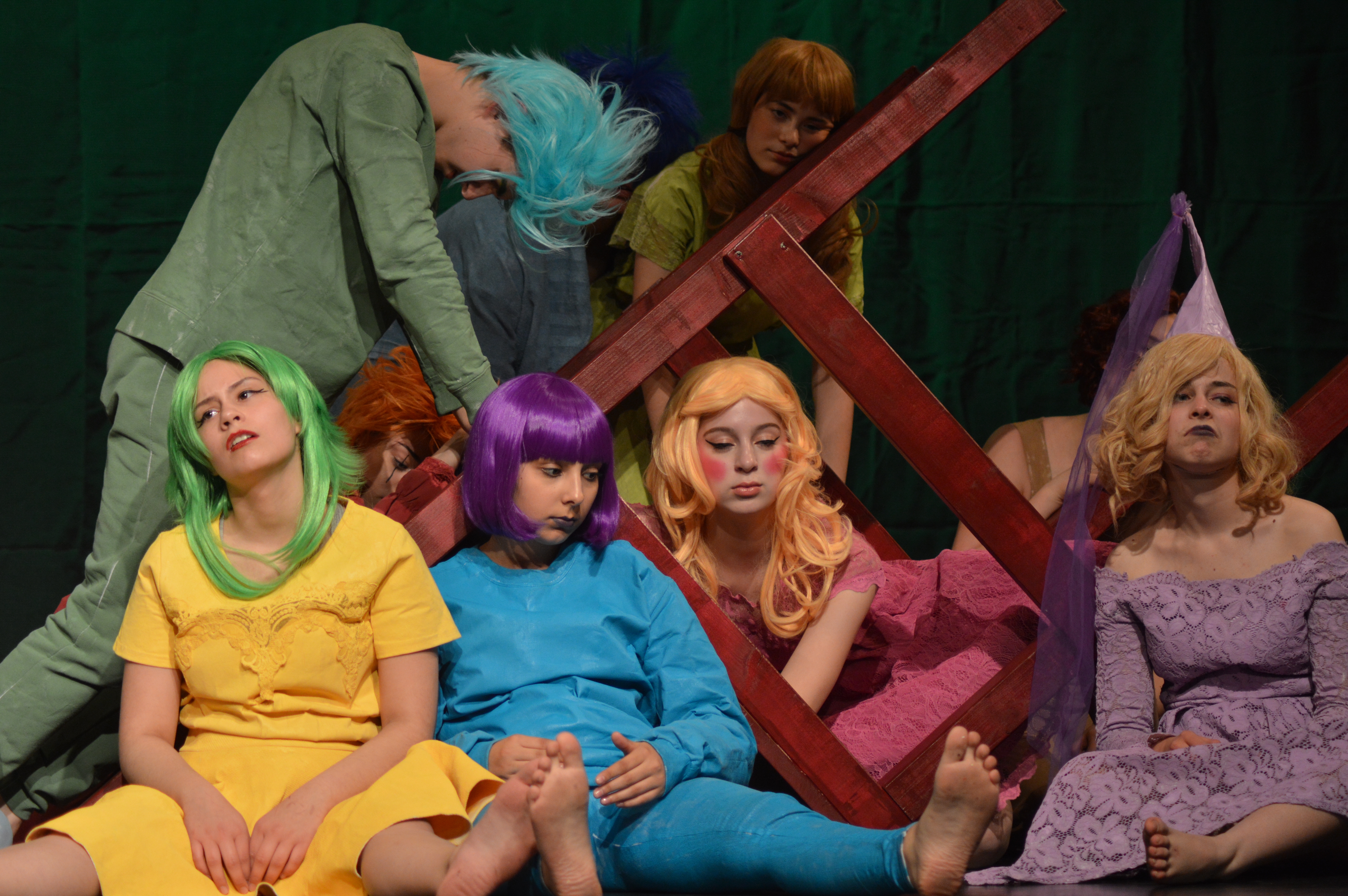 Theatre Week Korbach_gee whiz Four colourfully dressed youths with colourful wigs sit on the floor in front of a tilted huge chair