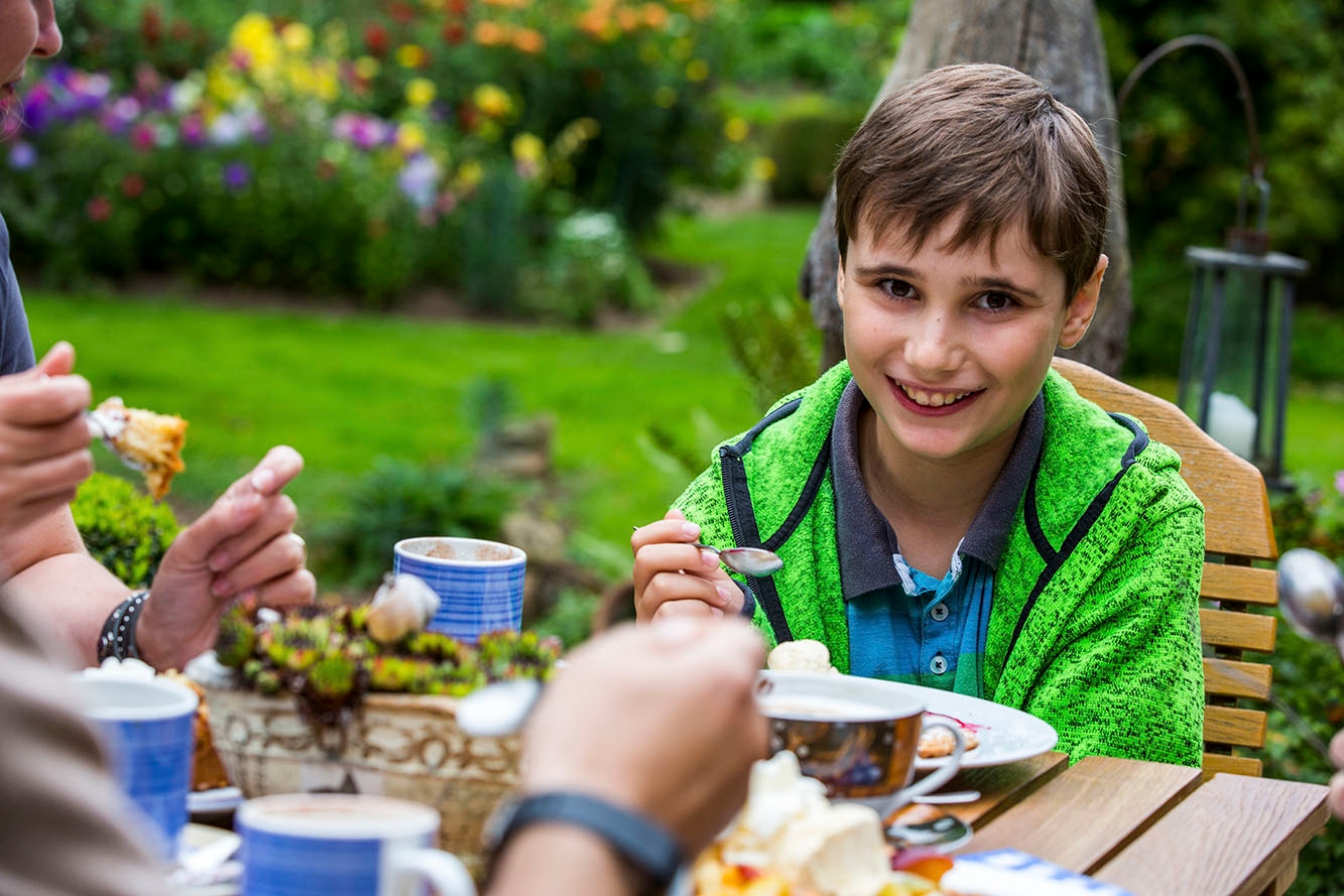 Bahçe masasında yemek yiyen gülümseyen çocuk