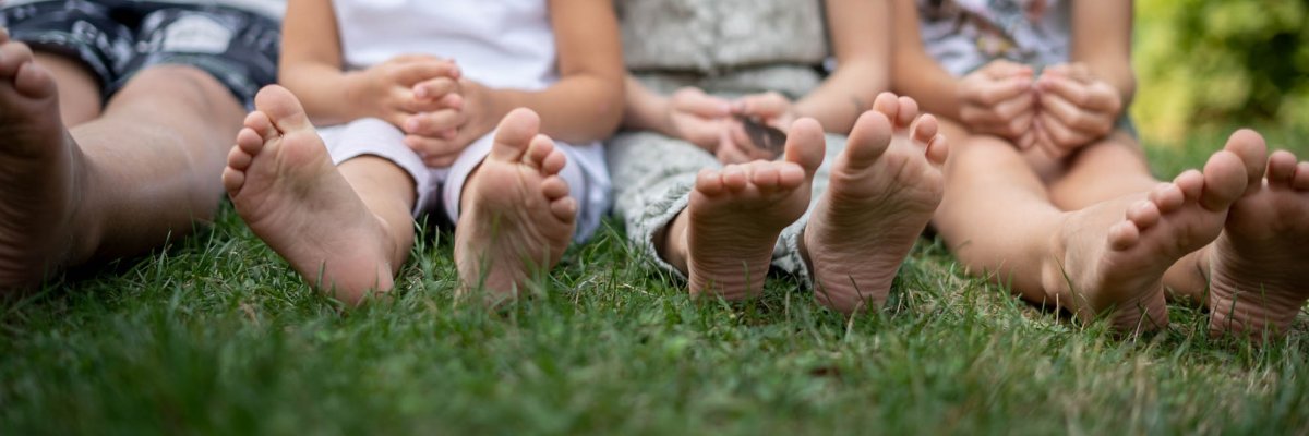 Çıplak ayaklarıyla çimlerin üzerinde oturan dört çocuk