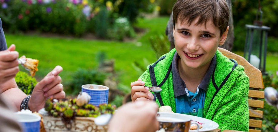 Усміхнений хлопчик їсть за садовим столом