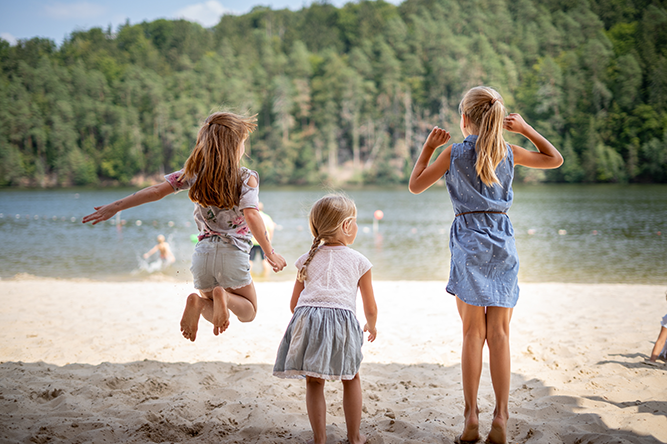 Дівчина на березі озера Три дівчинки стрибають на березі озера