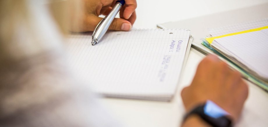 Eine Schülerin hält einen Stift und sitzt vor einem Block