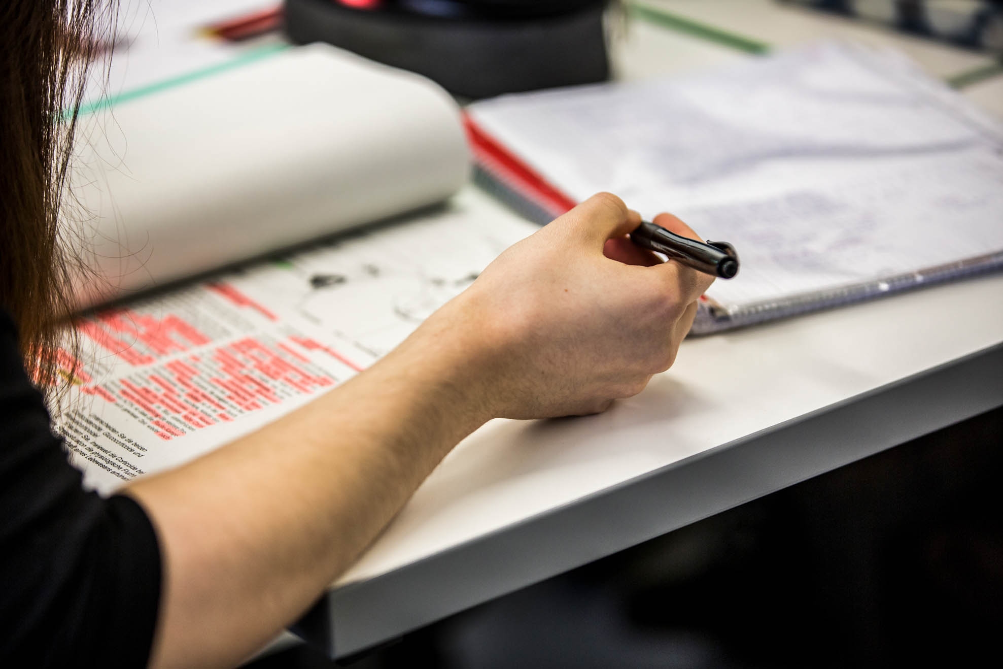 Schule Eine Schülerin liest in einem aufgeschlagenen Schulbuch, das auf dem Tisch vor ihr liegt