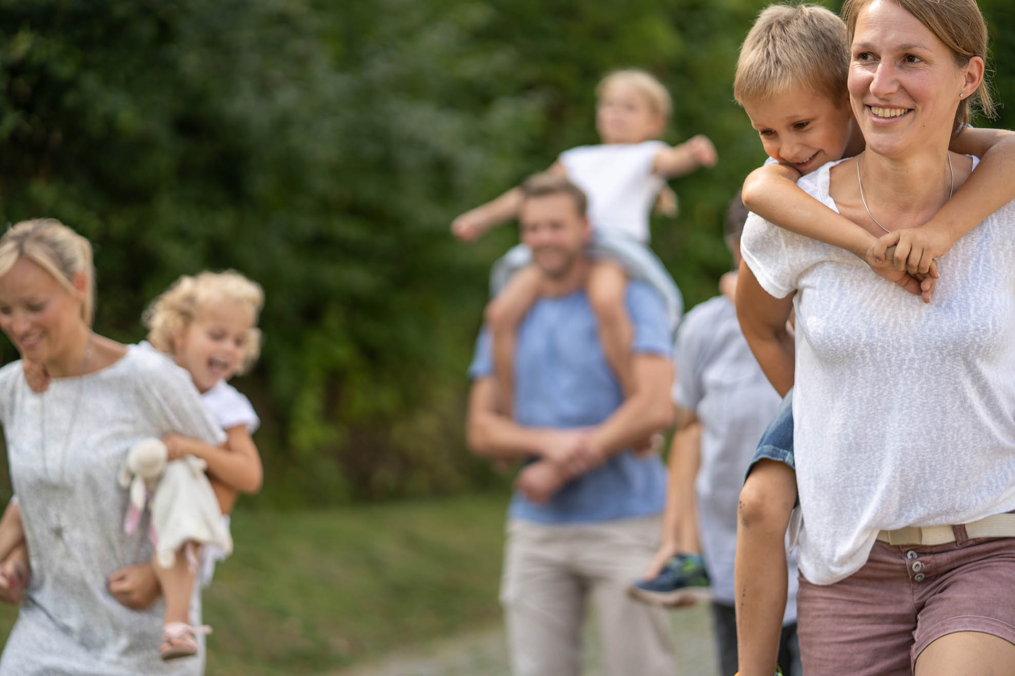 Familienausflug Zwei Frauen tragen zwei Jungen Huckepack und ein Mädchen sitzt auf den Schultern eines Mannes