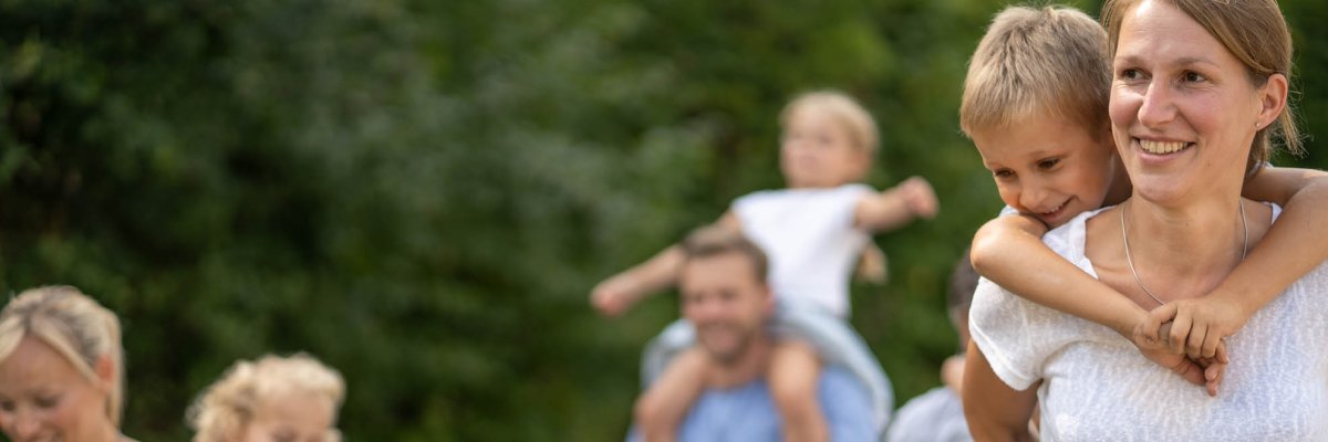 Zwei Frauen tragen zwei Jungen Huckepack und ein Mädchen sitzt auf den Schultern eines Mannes