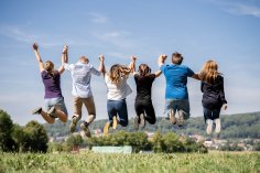 Sechs Jugendliche halten sich an den Händen und machen einen Luftsprung, Rückenansicht