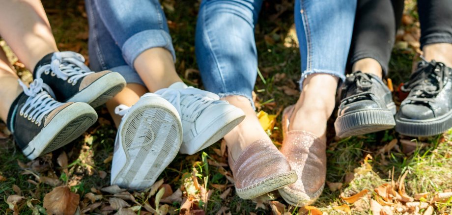 Drei Beinpaare auf dem Boden im Gras sitzend