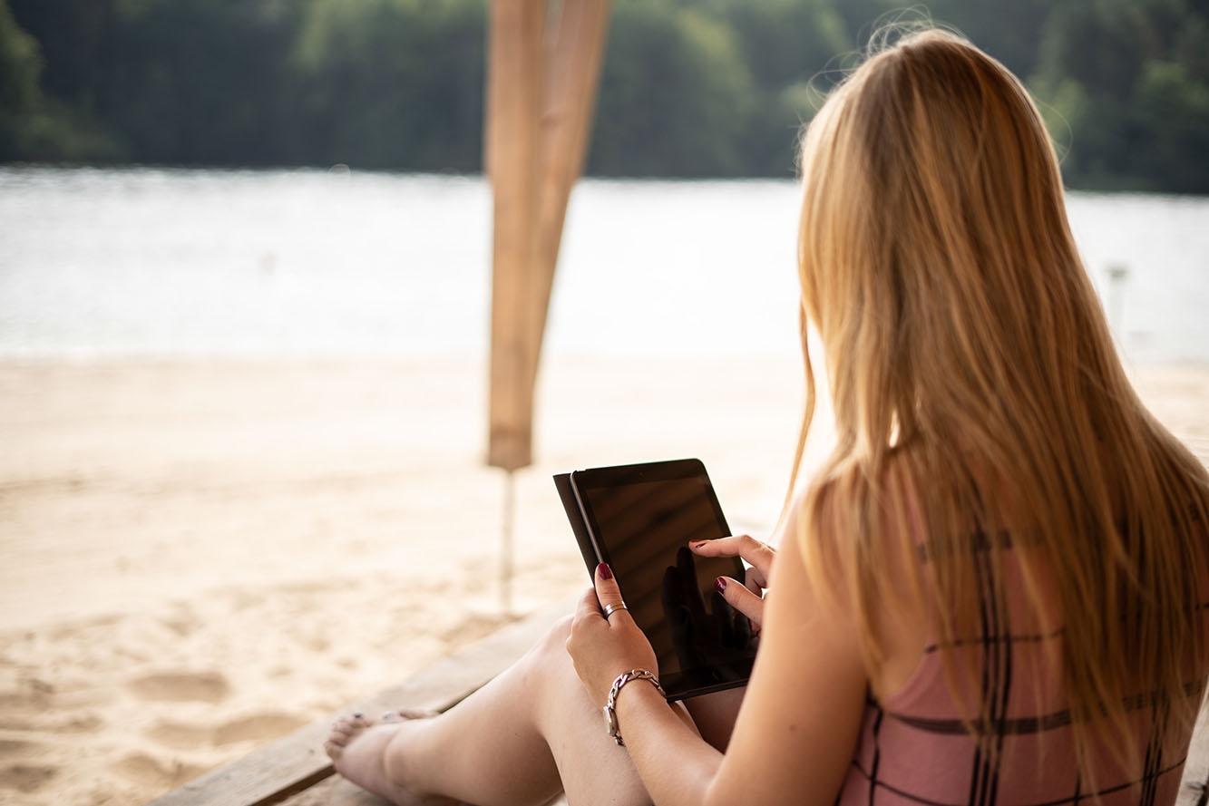 Frau mit langen blonden Haaren am Strand mit Tablet