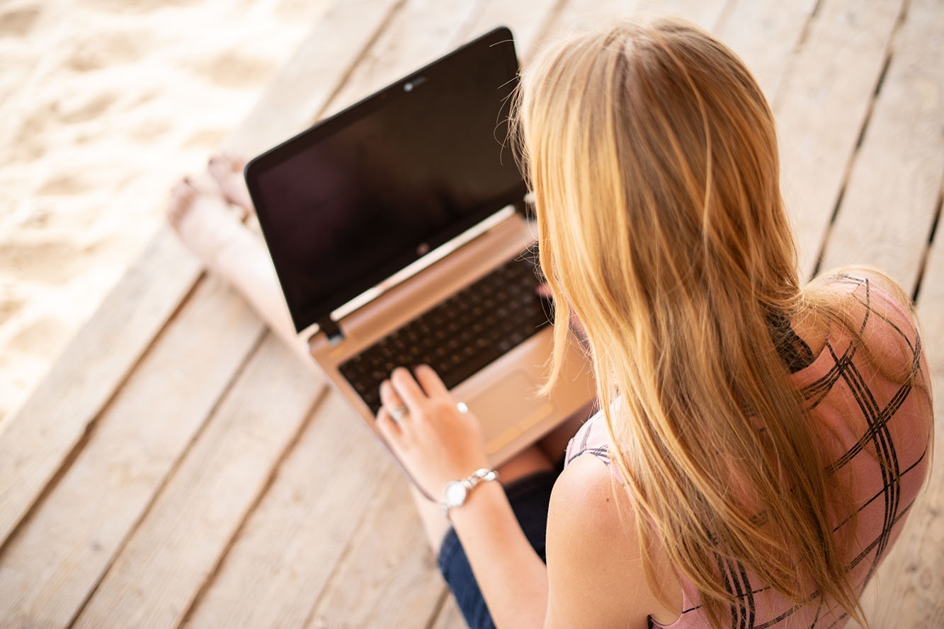 Digitalisierung Frau mit langen blonden Haaren sitzt auf Podium am Strand mit Notebook