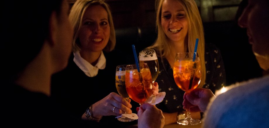 Drei junge Frauen mit orangefarbenen Getränken in einem dunklen Gastraum